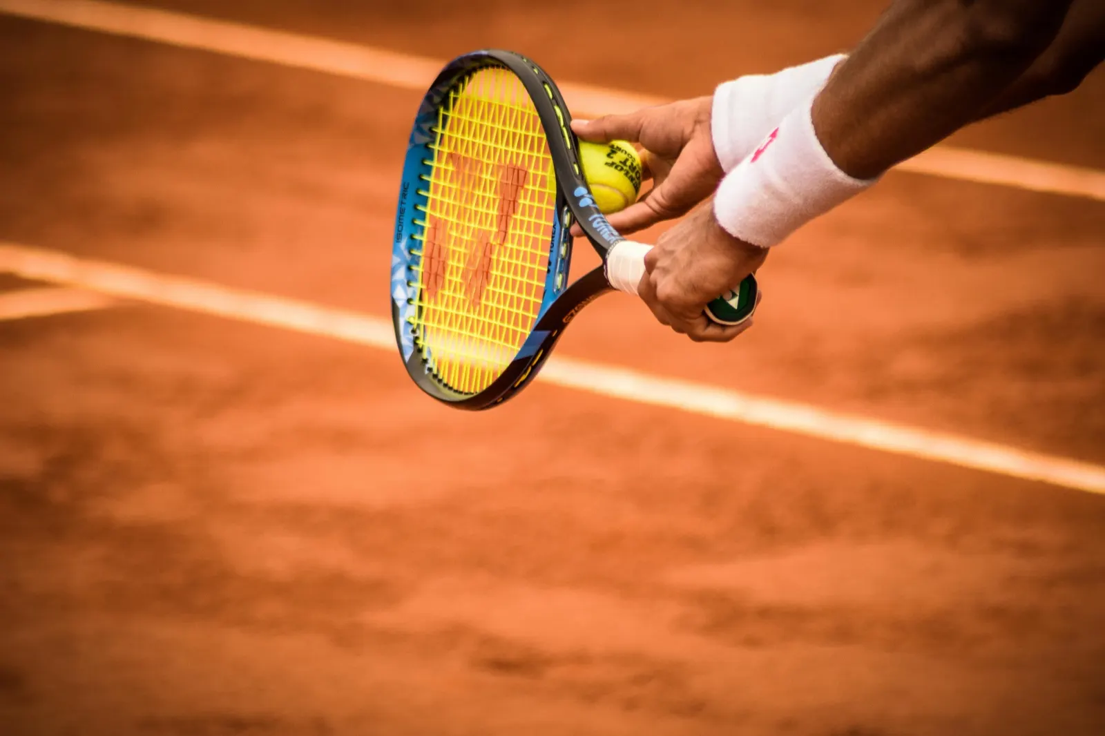 A tennis player holding a racket and ball on a clay court